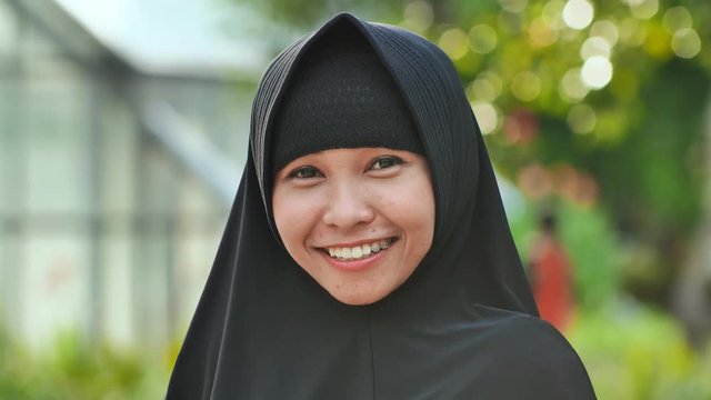 Portrait of a young smiling Muslim girl in a black hijab.