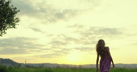 Rear of the little teen Caucasian blonde girl with long hair launching a plane toy model, then running away in the nice field lawn. Back view.