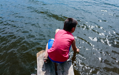 boy playing with water sitting on a wooden bridge on the shore of the lake, view from above