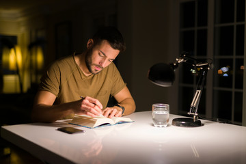 Young handsome man studying at home, reading a book at night