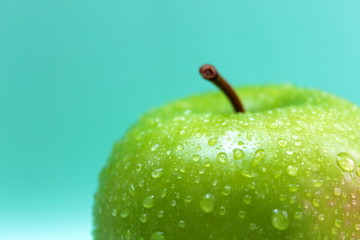 Green apple with numerous water drops on a blue background
