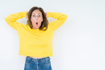 Beautiful middle age woman wearing yellow sweater over isolated background Crazy and scared with hands on head, afraid and surprised of shock with open mouth