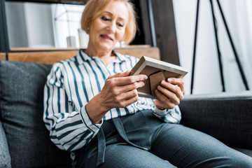 Obraz premium senior woman in casual clothes sitting on couch and looking at picture frame