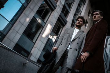 Two fashion men models posing on city street. Wearing in classic and casual closes. Suit, coat,...