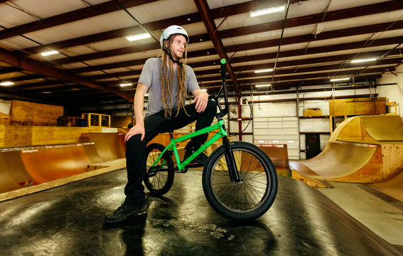 Portrait of a man with dredlocks and a helmet on a BMX bike at an extreme sports park