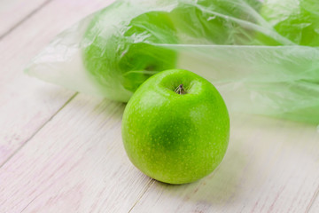 Fresh green apples in plastic bag on wooden table. environmental concept of non-ecological use of plastic
