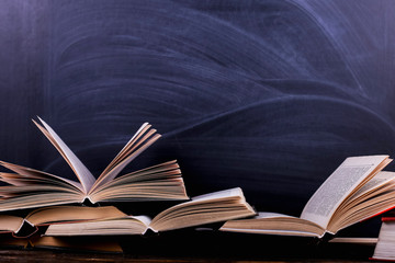 Open books are a stack on the desk, against the background of a chalk board. Difficult homework at...