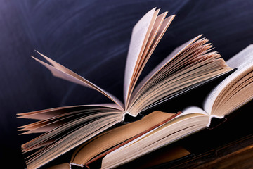 Open books are a stack on the desk, against the background of a chalk board. Difficult homework at school, a mountain of knowledge.