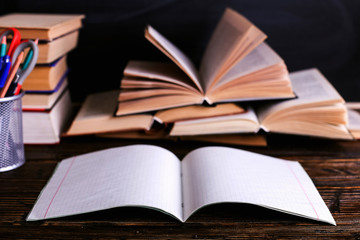 Notebook, open books and school supplies on a dark wooden table against the background of a chalk board. Education in school.