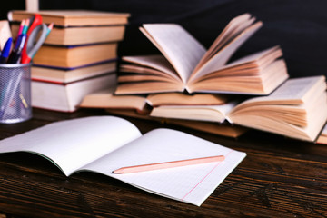 Notebook, open books and school supplies on a dark wooden table against the background of a chalk...