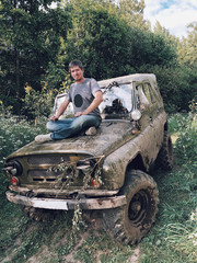 Fototapeta premium Young man sitting on a hood of off-road trophy car 4x4