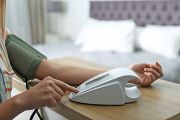 Fototapeta premium Woman checking blood pressure with sphygmomanometer at table indoors, closeup. Cardiology concept