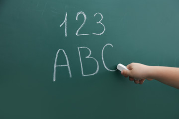 Little child writing letters and numbers on chalkboard, closeup