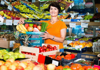 Obraz premium Smiling female is standing with basket with vegetables and fruits