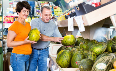 Fototapeta premium Adult male and female are choosing green melons in the store.