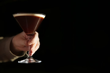 Barman holding espresso martini cocktail in darkness, closeup. Space for text