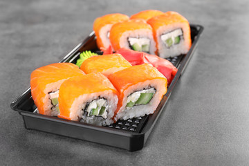 Box with tasty sushi rolls on grey table. Food delivery