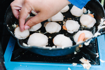 View of hand putting scallops in a cast iron pan to cook on camp stove