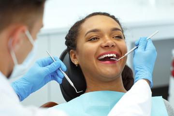 Woman sitting on dental chair, smiling while dentist cures her teeth.