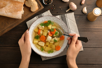 Young woman eating homemade chicken soup at table, top view