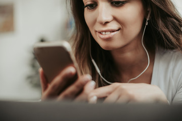 Close up of a girl holds phone in hands. She looks at it and smiles a bit. Woman is listening to music thourgh headphones. Cut view
