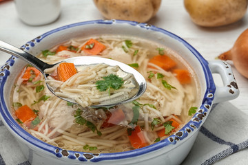 Spoon with fresh homemade chicken soup over dish, closeup