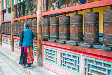 Woman Is Praying By Rotating Cylinders In Buddhist Temple.