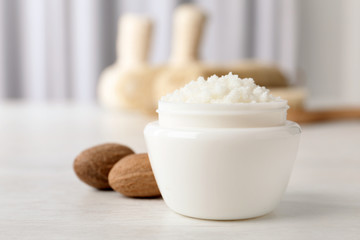 Jar of shea butter and nuts on table against blurred background. Space for text