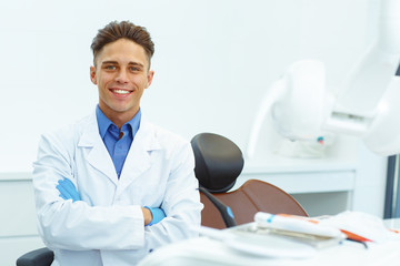 Young male dentist, standing with hand crossed, smiling and looking at camera.