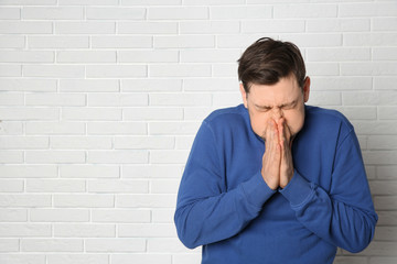 Mature man suffering from cold near brick wall. Space for text
