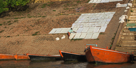 Sábanas tendidas en el suelo a orillas del río Ganges, junto a las barcas, en Varanasi, India,...