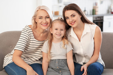 Portrait of young woman, her mature mother and daughter on sofa in living room