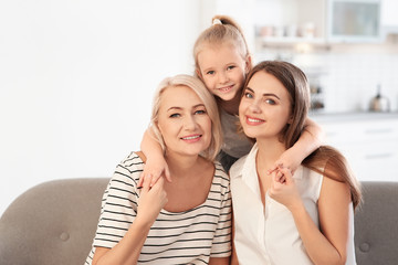 Portrait of young woman, her mature mother and daughter on sofa in living room