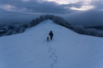 Young man trekking together with his dog through a cold winter day in the mountains of Romania
