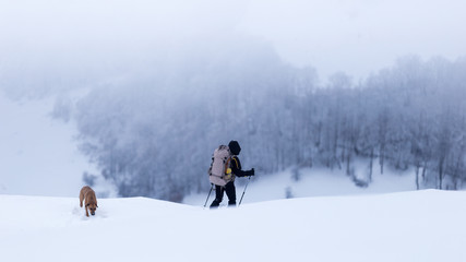 Young man trekking together with his dog through a cold winter day in the mountains of Romania