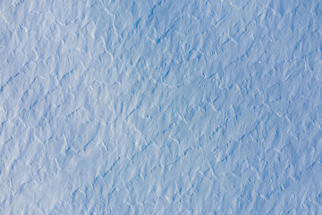 Aerial view of snow covered ground texture with rough wavy surface created by wind. Abstract winter background in blue tone