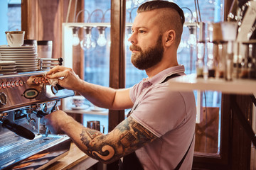 Stylish barista looking sideways while preparing a cup of coffee for a customer in the coffee shop
