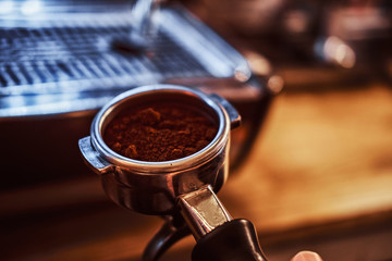 Close-up photo of a barista hand holding a portafilter with a black ground coffee in a cafe shop or restaurant