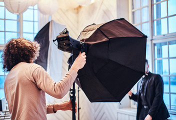 Photo of a curly photographer in a studio who turned his back and adjusts the light