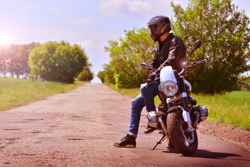 Stylish biker with motorbike stoped on a abandoned road. Motorcycle background.  Tonned.