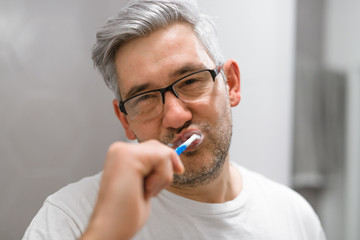 middle aged gray haired man brushing teeth in bathroom