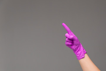 Hand in rubber glove points upwards with index finger. Neutral background , copy space.