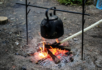 Rest on the nature, a black kettle is heated by water on a fire.