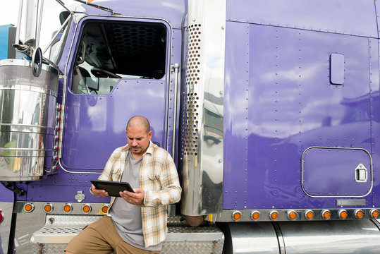Truck driver working on digital tablet by his semi-truck
