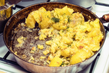 Fried potatoes with dill in a pan on gas stove