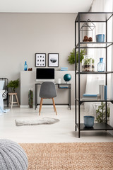 Metal shelf with cones, vases, plant and books in grey scandinavian home office with industrial desk with computer and copy space on the grey wall