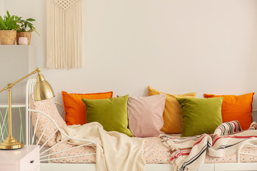 Golden lamp on the nightstand next to olive green, pastel pink, yellow and orange pillows on single...