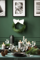 Vertical view of christmas garland and black and white posters on green wall of dining room set for christmas dinner