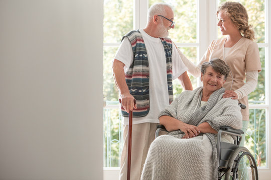Senior woman in wheelchair visited by her husband and nurse