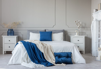 Grey, white and blue pillows and blanket on king size bed in elegant bedroom with copy space